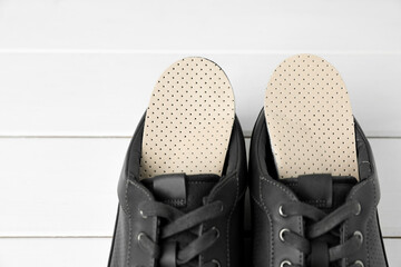 Orthopedic insoles in shoes on white wooden floor, closeup. Space for text