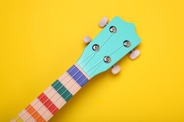 Head stock of colorful ukulele on yellow background, top view. String musical instrument