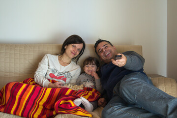 Image of a smiling family lying on the sofa at home watching a movie on TV and eating popcorn. Relaxed family evening

