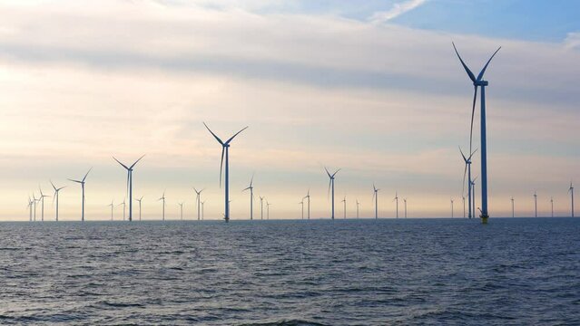Windmill park in the sea, View of windmill turbines generating green energy electric in the Netherlands. Offshore farm windturbines against blue sky.