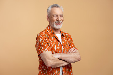 Portrait of handsome senior man standing with arms crossed isolated on beige background