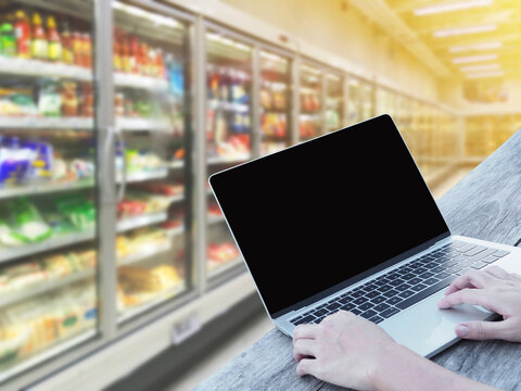 hand typing laptop over supermarket blur background, online shopping concept.