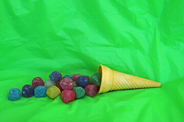 Horizontal side view of ice cream cone on its side with gummy candy spilling out onto bright green table and background with copy space.
