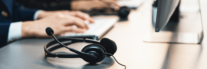 Panorama focus headset on call center workspace desk with blur background of operator team or...