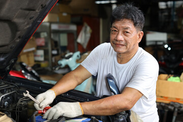 Man technician car mechanic in half uniform checking maintenance a car service at repair garage station. Worker holding wrench and fixing breakdown vehicle. Concept of car center repair service.