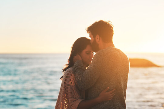 Sunset, beach and couple kiss forehead for relax, bonding and quality time on romantic date. Nature, travel and man and woman embrace for anniversary or honeymoon on holiday, weekend and vacation