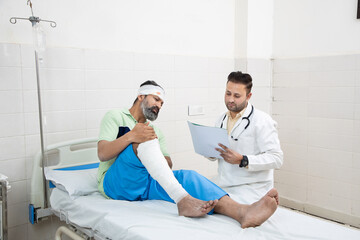 Indian patient with bone fracture listening to, Young injured man with broken leg talking to...
