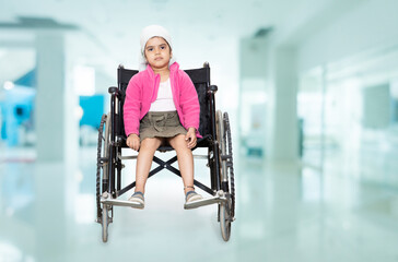 Young indian handicapped girl kid sitting on a wheelchair at hospital. Healthcare concept. Copy...