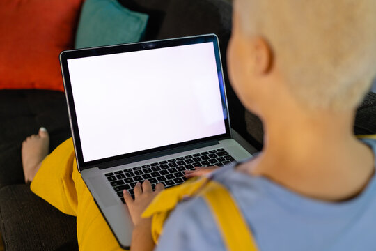Biracial woman sitting on sofa and using laptop with copy space on screen