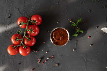 red chili sauce, tomato, sprig of parsley and peppercorns on a black background. top view