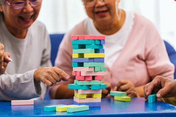 Fototapeta premium Senior people playing a wooden block tower, risk and strategy of project management. Concept of business risk with domino blocks. Older People playing jenga block removal game on table at home
