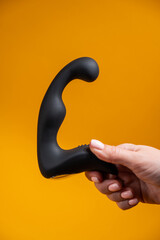 Woman holding black prostate massager on orange background. 