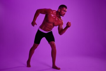 Man athletic body bodybuilder in briefs with nude torso abs full-length in the background fitness classes, purple colored light. Advertising, sports, active lifestyle, competition, challenge concept. 