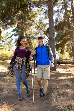 Happy biracial couple wearing backpacks and hiking in forest