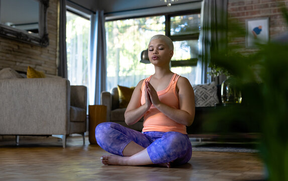Tranquil unaltered biracial woman practicing yoga meditation sitting in living room at home