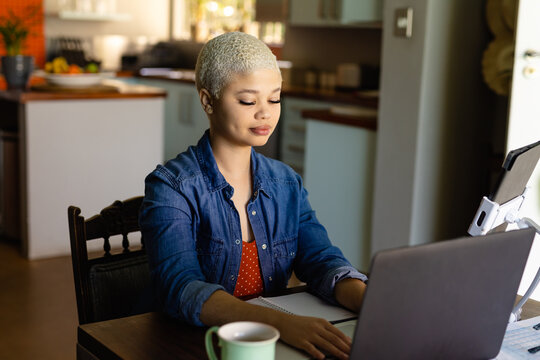 Happy biracial woman sitting at table using laptop and working