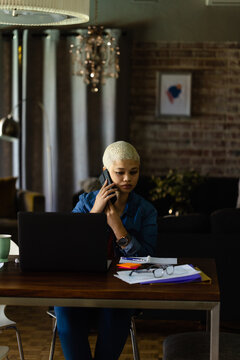 Unaltered biracial casual businesswoman talking on smartphone in home office dining room, copy space