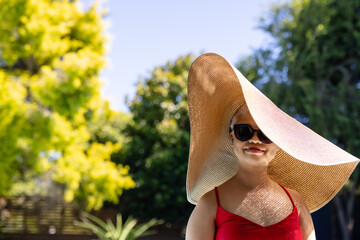 Unaltered portrait of biracial woman in sunhat, sunglasses smiling in sunny garden, copy space
