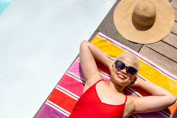 Overhead of happy fashionable unaltered biracial woman in sunglasses sunbathing by pool, copy space