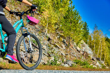 Naklejka premium Part of a bicycle and a woman in a tracksuit rides along a mountain road. Girl Athlete cyclist travels through mountainous terrain, stopped at the side of the road