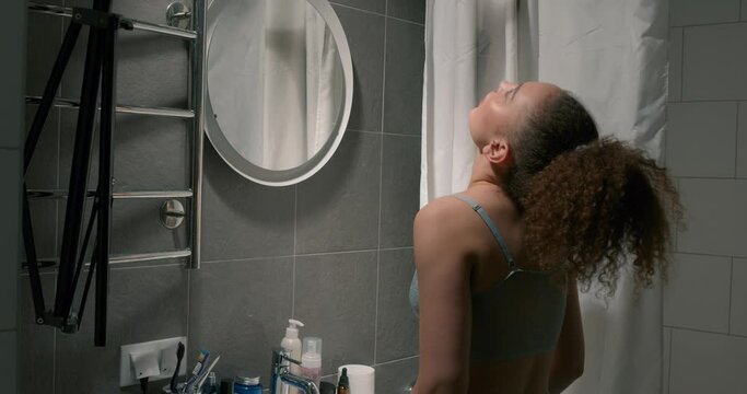 young woman rinsing teeth after brushong them. back view, girl in shorts and blue top gargling throat in the bathroom in the morning