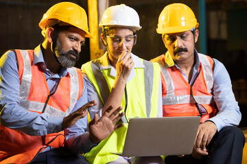 Team of young indian engineers wearing safety helmets and vest working together on a project at...