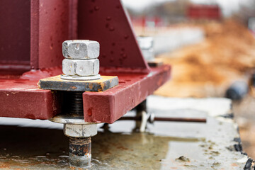 Installation of a metal column for an industrial building. Mounting bolts close-up. Connection of a structure with a reinforced concrete foundation. Anchor bolt.
