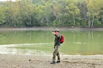 hombre adulto con una mochila roja haciendo fotos y shelfies en un bosque con un lago en Marbella España