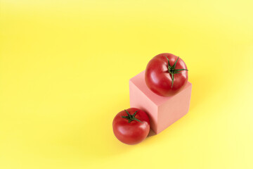 Two fresh tomatoes and a pink podium on a yellow background