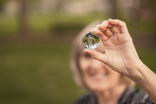 View of crystal ball with upside down reflection of  smiling woman holding it; grass and trees in background