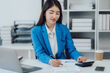 Asian Business woman using calculator and laptop for doing math finance on an office desk, tax, report, accounting, statistics, and analytical research concept