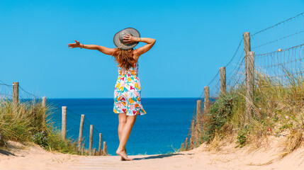 Woman wearing dress with open arms standing in sand dune enjoying beautiful sea and beach view- Atlantic ocean in France