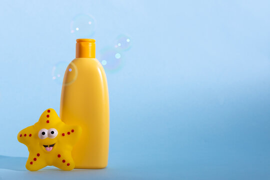 Yellow plastic bottle with baby cosmetic and funny bath toy. Soap bubbles on a background. The concept of children's bath time.