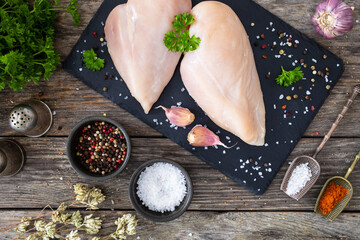 Fresh raw chicken breasts on cutting board with spices on wooden background

