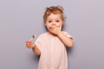 Surprised little girl holding toothbrush isolated on gray background learning daily dental hygiene holding toothbrush, kid's health and wellness, copy space for promotion.