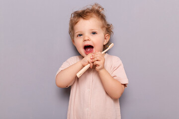 Healthy mouth and lifestyle from an early age. Funny little girl holding toothbrush isolated on gray background standing with open mouth holding toothbrush.