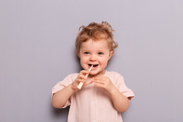 Everyday routine. Regular oral cleaning and dentistry for children. Smiling cheerful little girl holding toothbrush isolated on gray background,