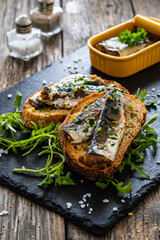 Tasty sandwiches - toasted bread with smoked sardine and arugula on wooden table - obrazy, fototapety, plakaty