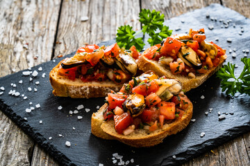 Tasty sandwiches - toasted bread with tomatoes and mussels on wooden table
