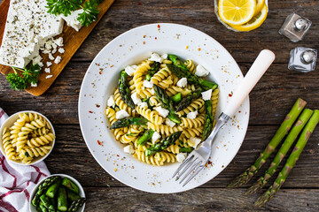 Noodles with asparagus and feta cheese on wooden table