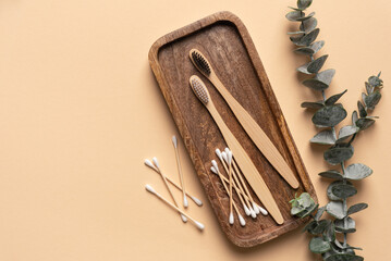 Eco-friendly bamboo toothbrushes, cotton buds and eucalyptus leaf on yellow background