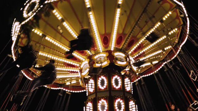 An old chain carousel in the park in close-up. Traditional fairground carousel at night. Amusement park. A carousel with lights and happy people