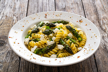 Noodles with asparagus and feta cheese on wooden table
