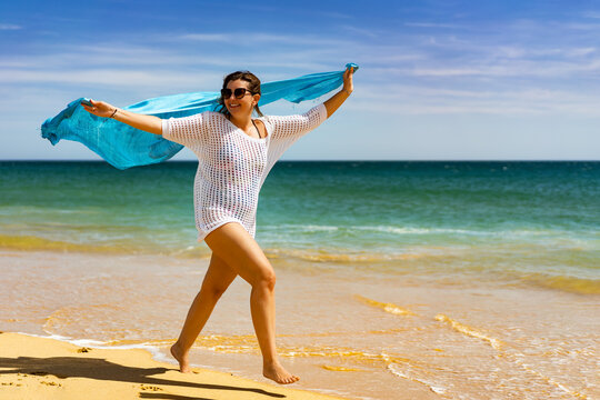 Beautiful woman walking on sunny beach holding shawl
