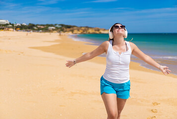 Beautiful woman walking on sunny beach listening to music
