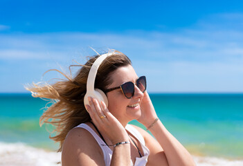 Beautiful woman walking on sunny beach listening to music
