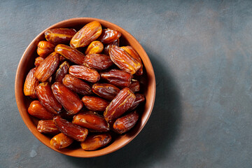 Pitted dates on a clay plate. Bowl with delicious dried dates on a dark background. Ramadan kareem. Top view. Copy space