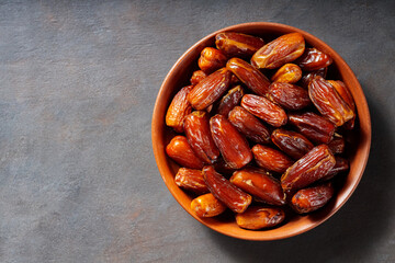 Pitted dates on a clay plate. Bowl with delicious dried dates on a dark background. Ramadan kareem. Top view. Copy space