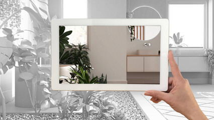 Augmented reality concept. Hand holding tablet with AR application used to simulate furniture and design products in total white unfinished background, urban jungle bathroom