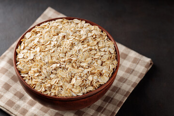 Oat flakes in bowl on a linen napkin. Raw oatmeal on a dark background. Vegan food concept